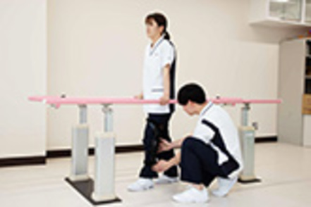 秋田大学 【理学療法学専攻】膝関節の手術後を想定して、膝に装具を装着し平行棒内で歩行練習を行っています。